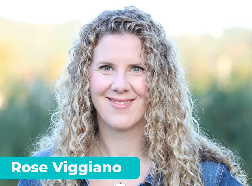 TraumaSolutions A woman with long curly blonde hair smiles outdoors, radiating warmth as she wears a denim shirt and a necklace—capturing a moment in her Search for Connection. The name "Rose Viggiano" appears in white text on a teal label in the lower left corner.